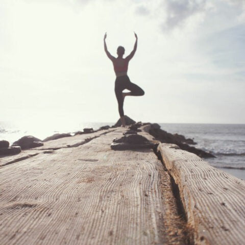 person standing in tree pose at the end of a pier