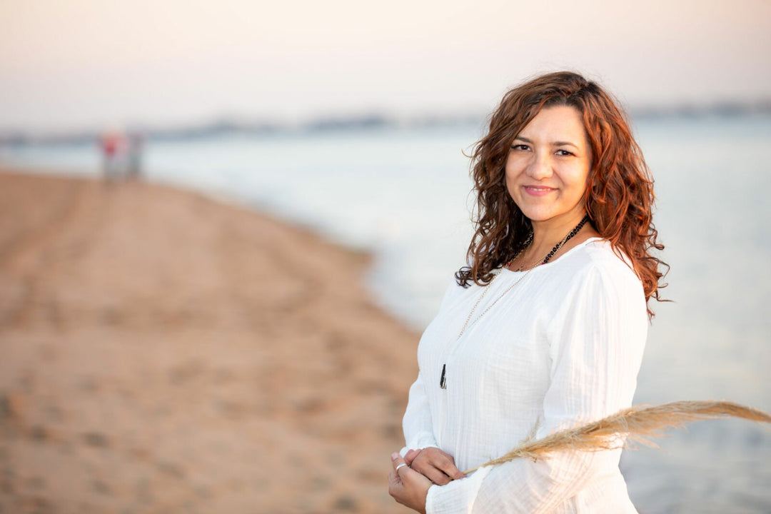 Smiling woman in white dress holding pampas grass on a sandy beach at sunset