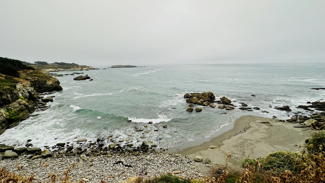 Rocky coastline with sandy beach, ocean waves, and cloudy sky, tranquil nature scene