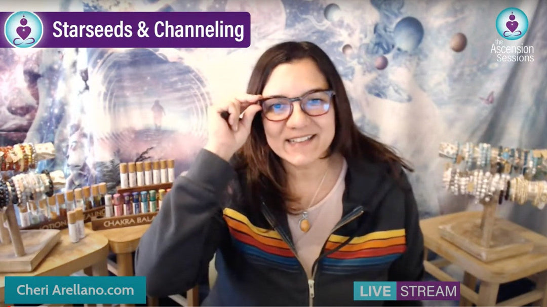 Smiling woman with glasses hosting live stream on starseeds and channeling, jewelry and chakra oils displayed, cosmic background.