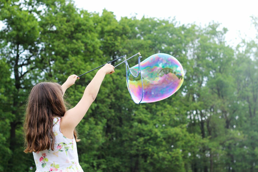 Girl creating giant iridescent bubble outdoors with trees, symbolizing light, joy, and ascension energy