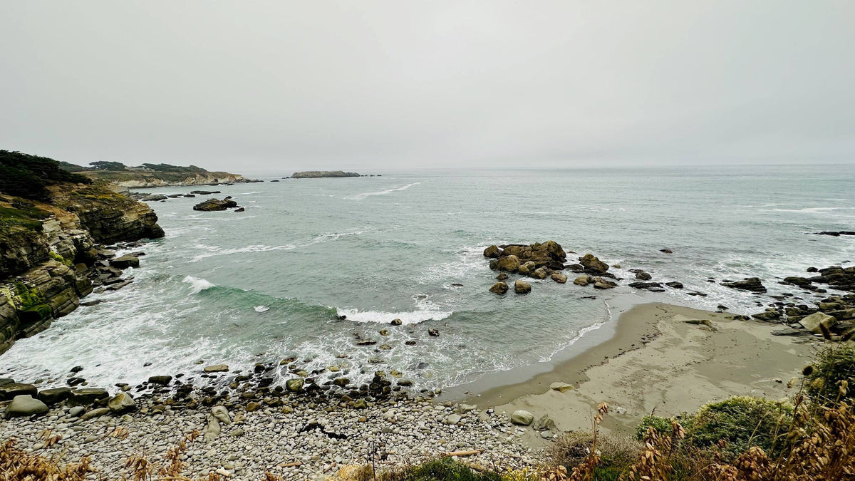 Serene coastal scene with misty ocean, rocky cliffs, and pebble beach — perfect for spiritual healing and ascension journeys.