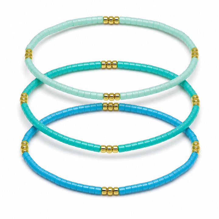 Three beaded stretch bracelets in mint green, turquoise, and royal blue, each accented with small gold bead clusters, arranged on a white background.