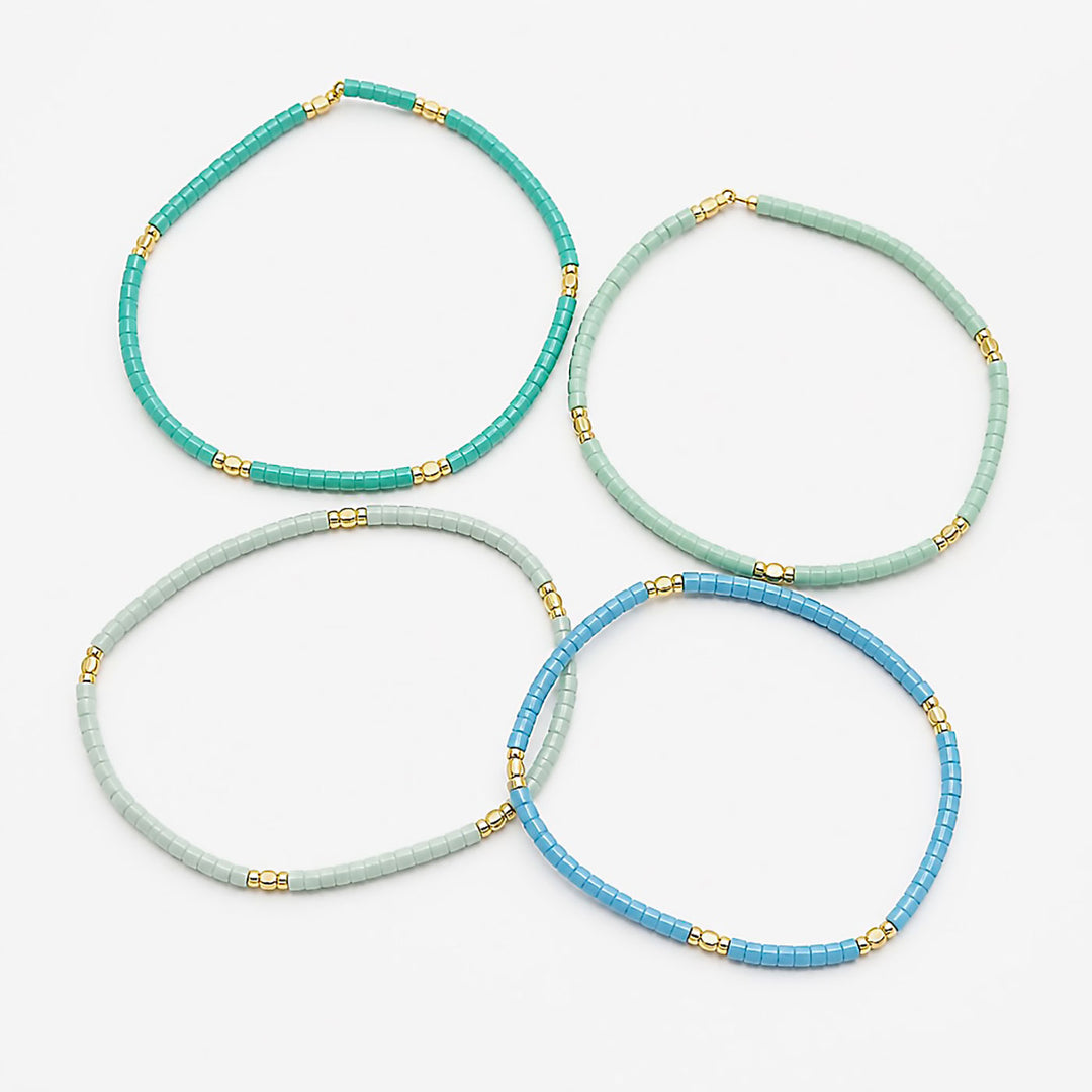 Four beaded necklaces in shades of turquoise, mint green, pale blue, and medium blue, accented with small gold spacer beads, arranged on a light gray background.