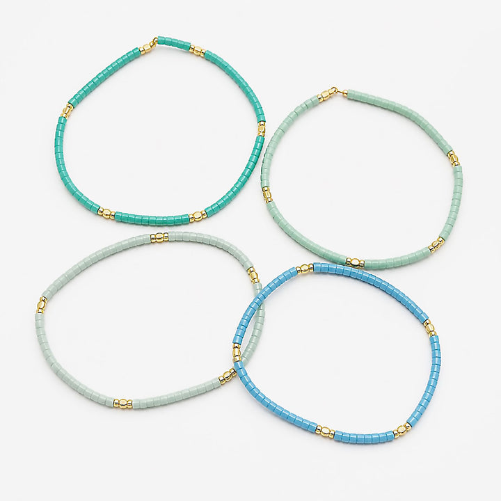 Four beaded necklaces in shades of turquoise, mint green, pale blue, and medium blue, accented with small gold spacer beads, arranged on a light gray background.