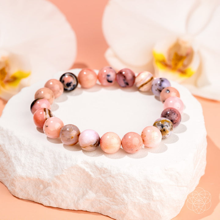 Beaded bracelet with pink and brown stones on a white surface with flowers in the background