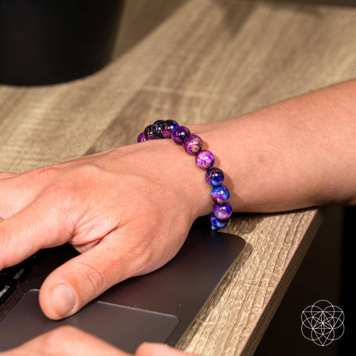 Hand using a computer mouse with a colorful beaded bracelet on a wooden surface