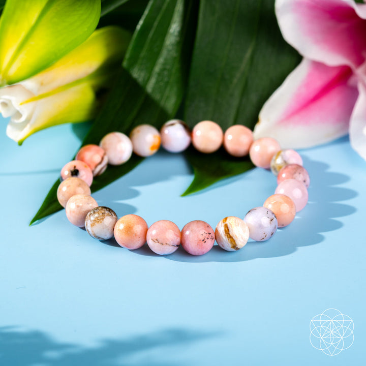 Beaded bracelet with pink and white stones on a blue surface with flowers in the background
