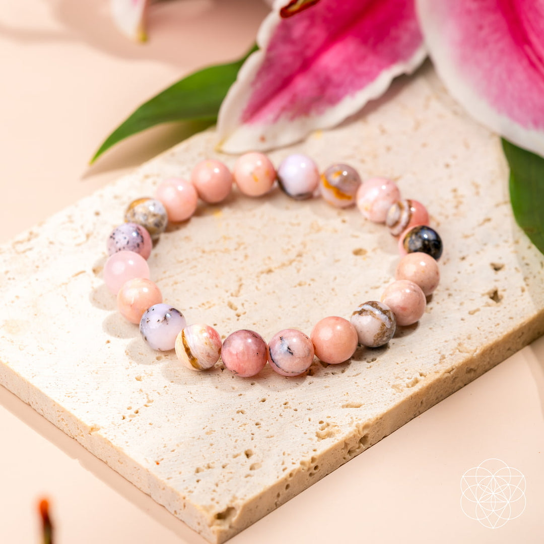 Necklace with multicolored beads on a textured surface with pink flowers in the background