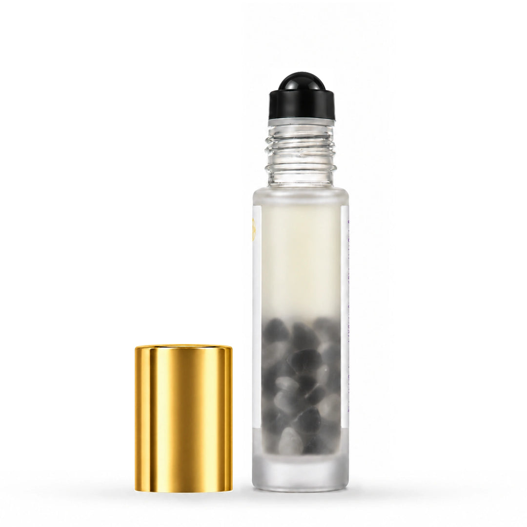 A clear glass roller bottle with a black spherical cap and a separate shiny gold cap, shown on a clean white background.