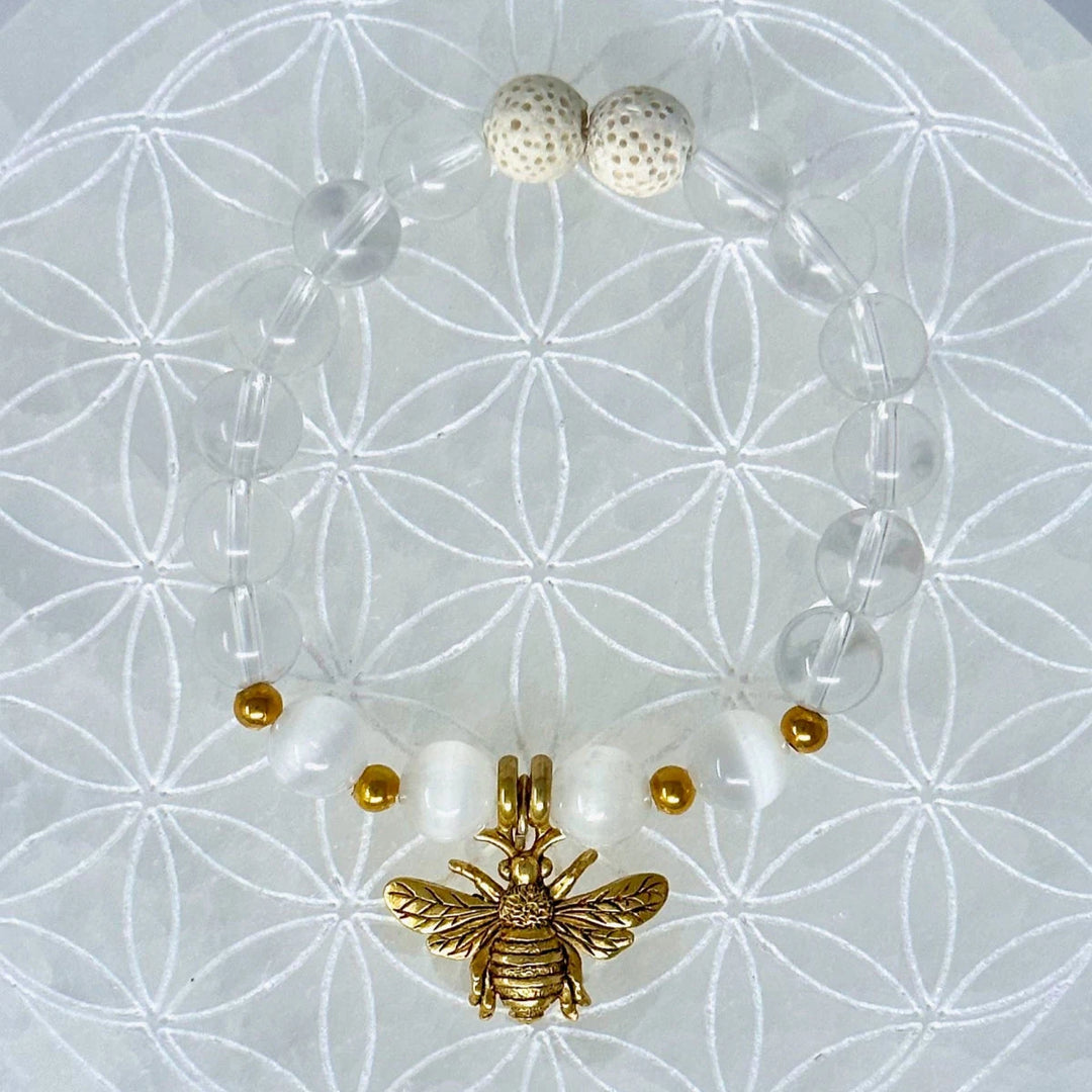 Golden bee pendant bracelet with clear and white beads on sacred geometry background