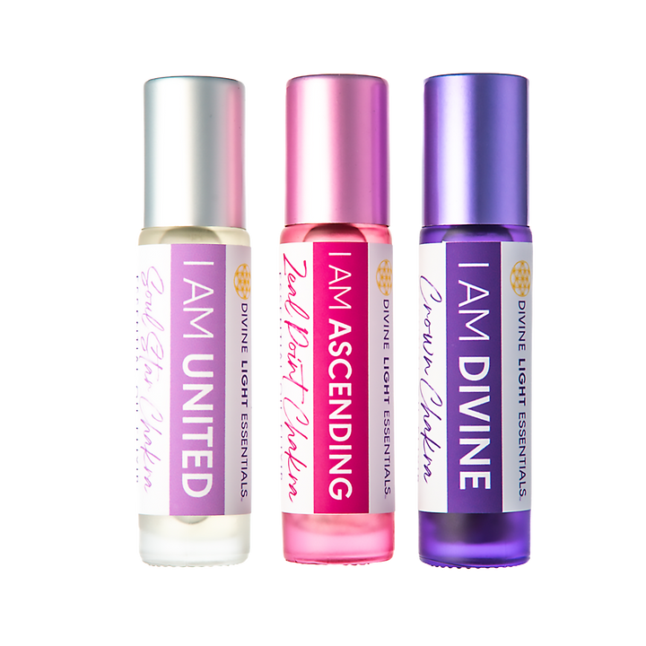 Three Divine Light Essentials roll-on essential oil bottles in silver, pink, and purple caps with white and purple labels, shown on a white background.