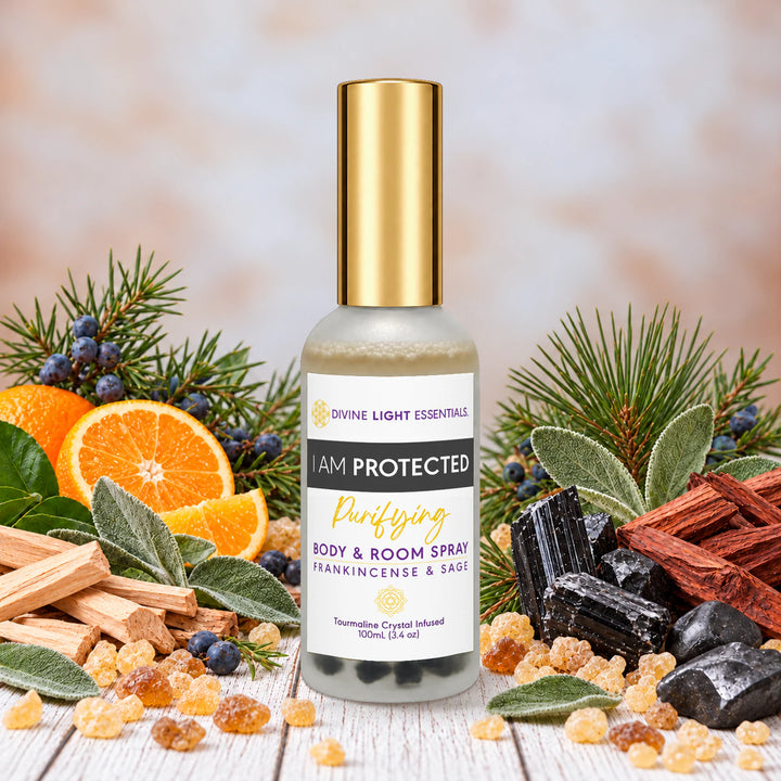 I Am Protected spray with a gold cap, surrounded by juniper berries, sage, pine, sandalwood, rosewood, wild orange, frankincense resin, black tourmaline and shungite on a pale wood surface.