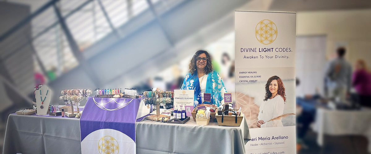 Cheri Arellano behind a Divine Light Codes display of crystal jewelry and elixirs at an indoor event.