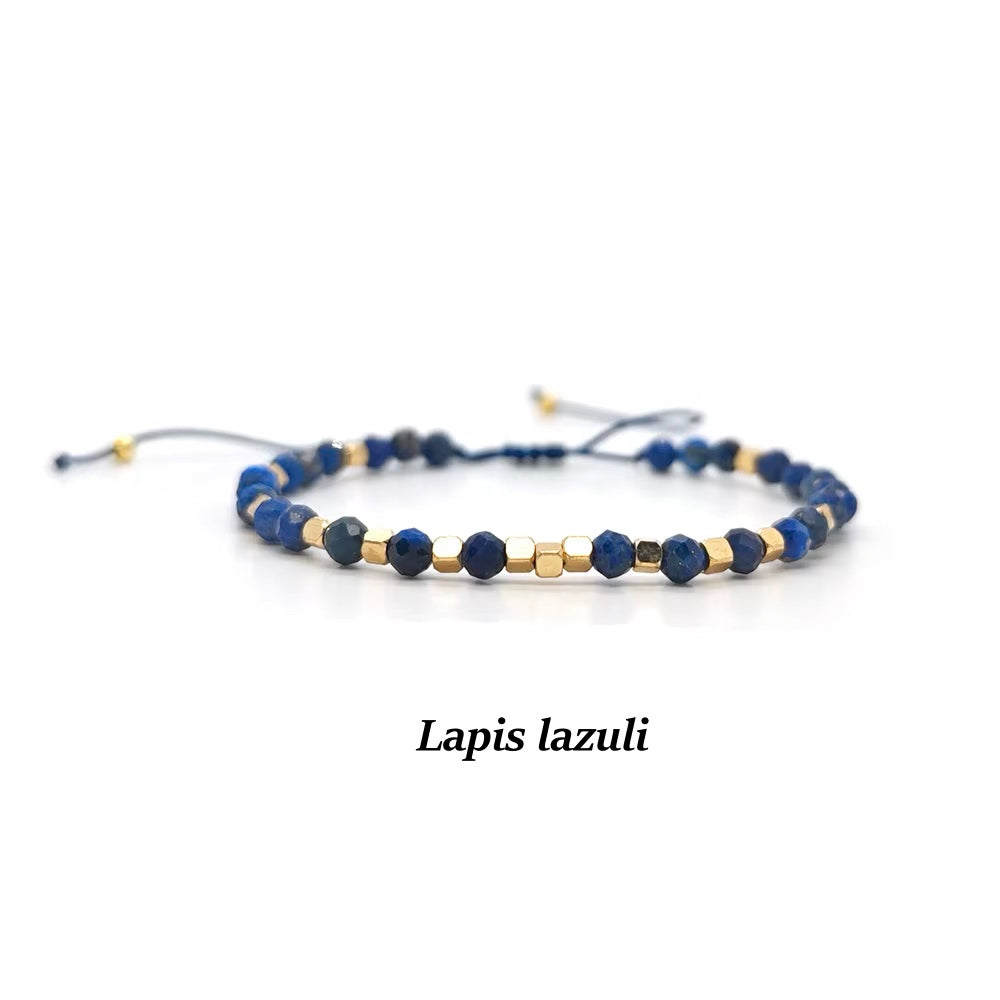 A beaded adjustable cord bracelet made of deep blue lapis lazuli stones and small gold spacer beads, displayed on a clean white background with the text &