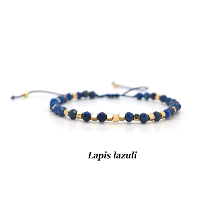 A beaded adjustable cord bracelet made of deep blue lapis lazuli stones and small gold spacer beads, displayed on a clean white background with the text &