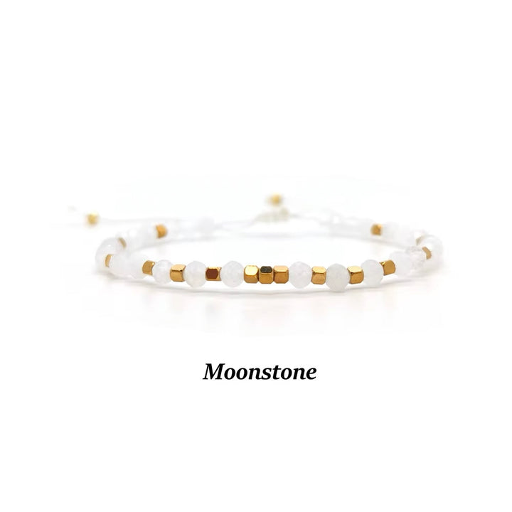 A delicate beaded bracelet featuring white moonstone beads and small gold cube beads, displayed on a clean white background with the text &