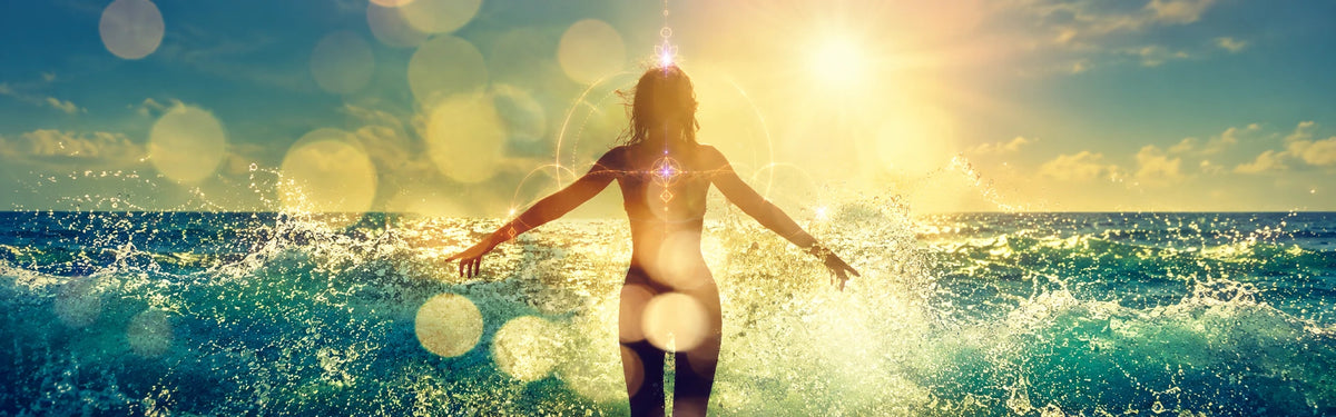 Woman standing with open arms in sparkling golden ocean waves and subtle light codes; desktop hero.