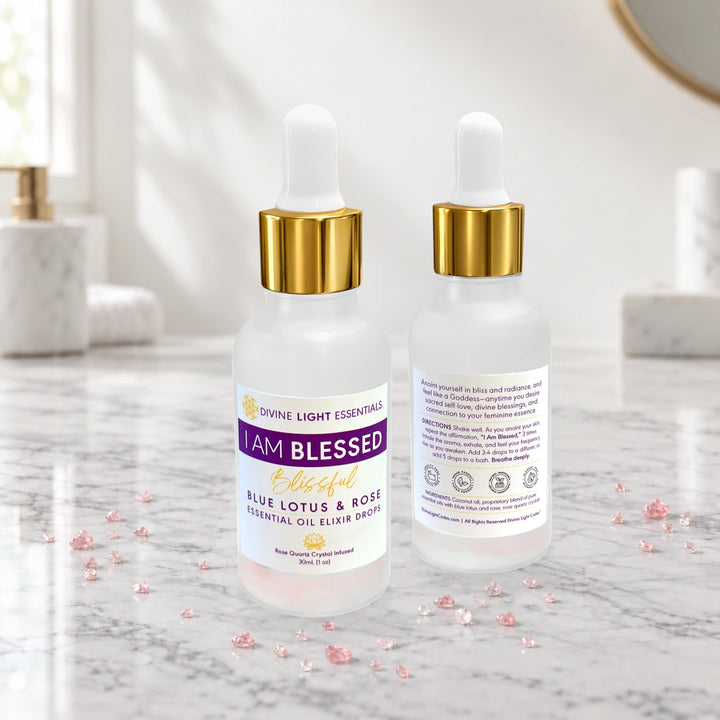Two frosted glass dropper bottles of Divine Light Essentials Blue Lotus &amp; Rose Essential Oil Elixir shown on a marble surface, with one bottle displaying the front label and the other showing the back packaging.
