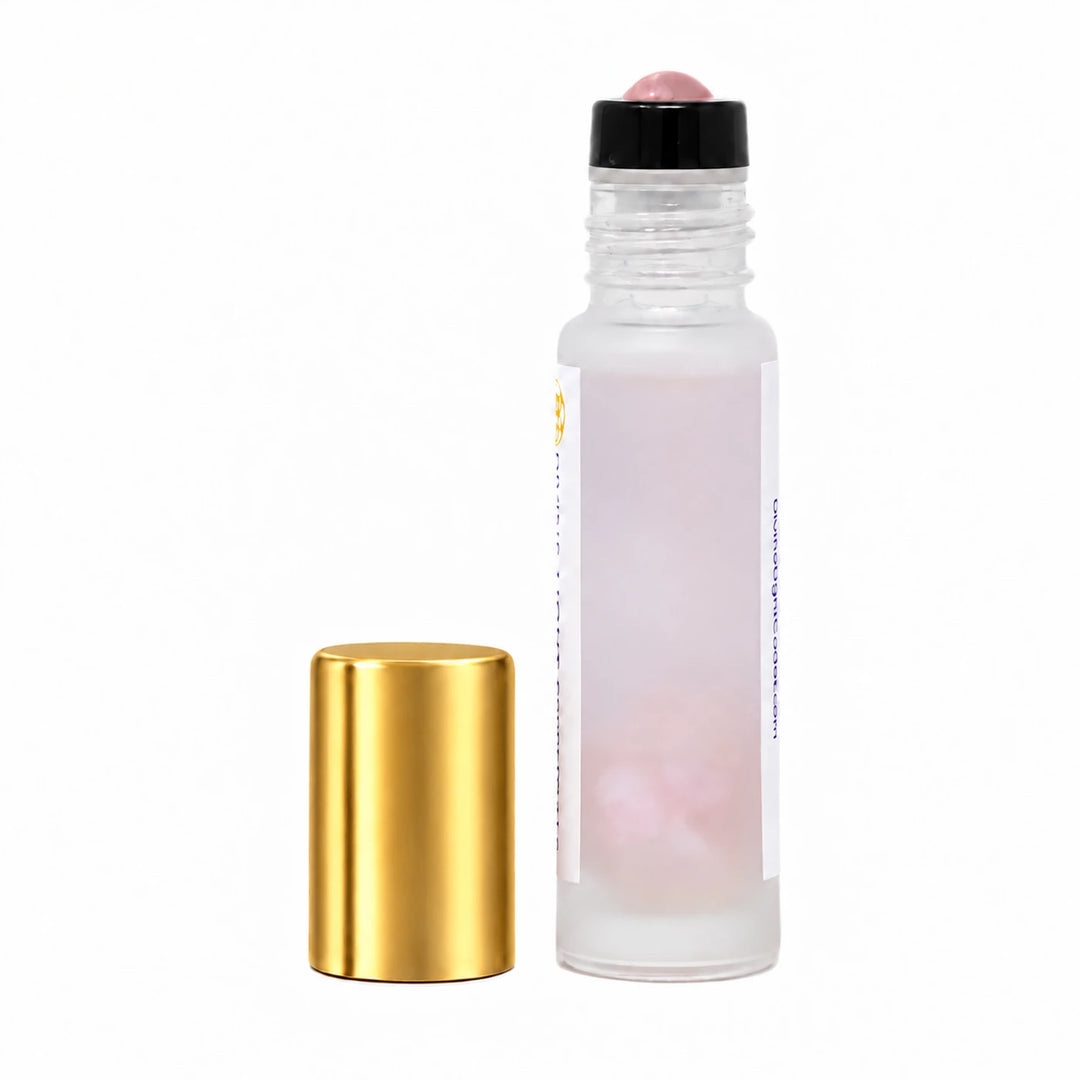 A clear glass roller bottle with a frosted finish, filled with pale pink liquid, shown next to its detached metallic gold cap on a plain white background.