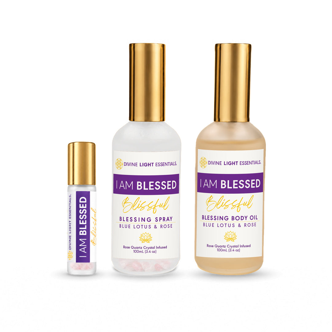 Three Divine Light Essentials 'I Am Blessed' fragrance products on a white background: a small roller bottle, a body oil bottle, and a spray bottle, all with gold caps and cream-colored labels with purple and gold text.
