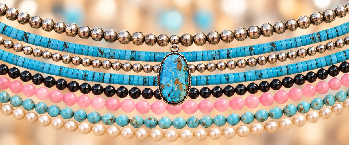 Horizontal strands of colorful beads with a turquoise pendant against a softly blurred background.