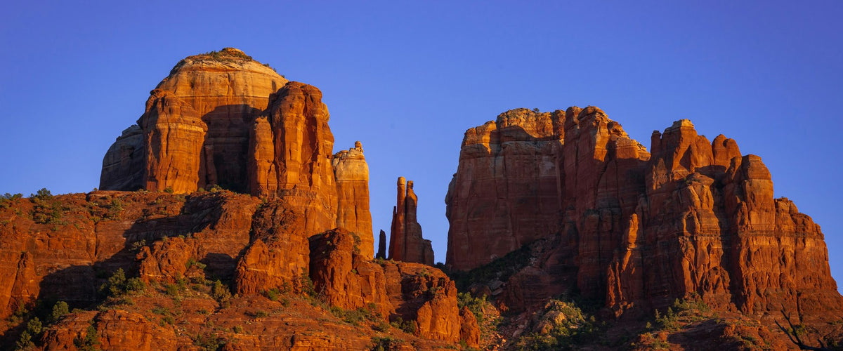 Sunlit red sandstone towers of Cathedral Rock beneath a clear blue sky in Sedona, Arizona.