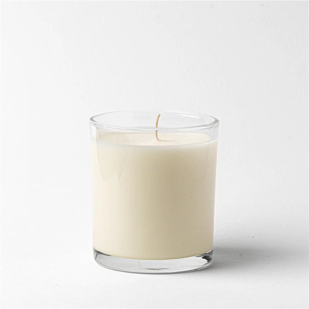 Glass candle with a white candle inside on a light gray background