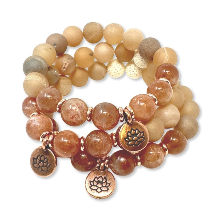 Stack of sunstone beaded bracelets with bronze lotus charm on a white background