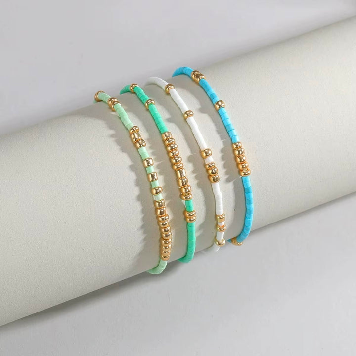 Four beaded stretch bracelets in mint green, turquoise blue, and white, accented with gold spacer beads, displayed on a light gray cylindrical mannequin arm.