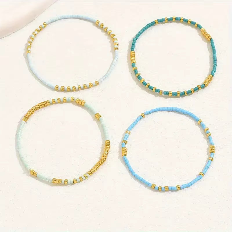 Set of four beaded bracelets in light blue, turquoise, and gold on a white background