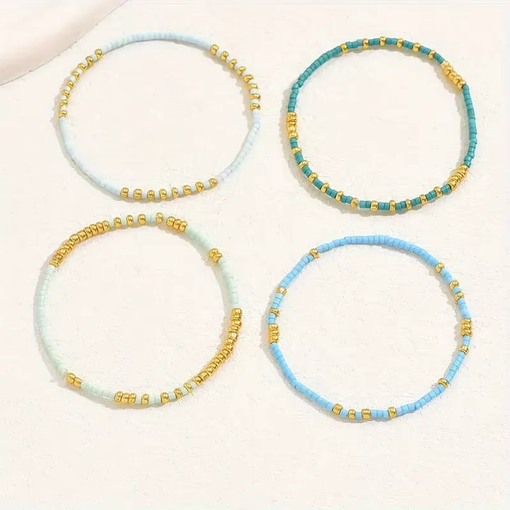 Set of four beaded bracelets in light blue, turquoise, and gold on a white background