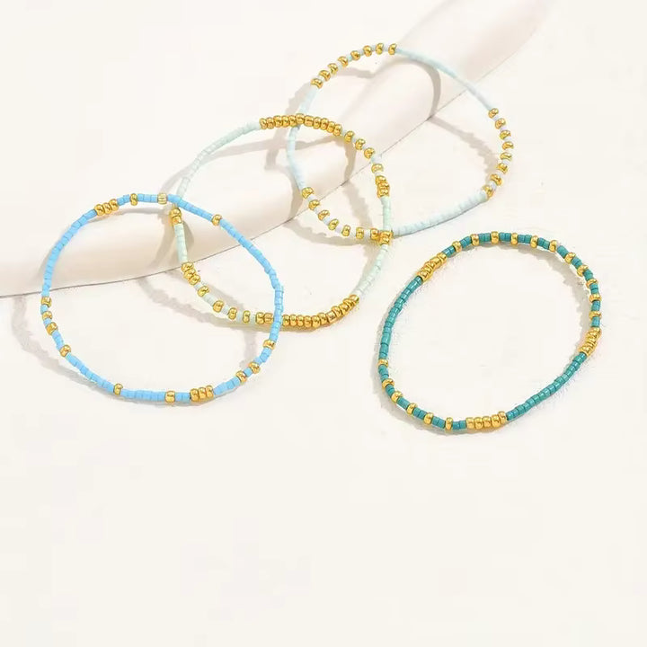 Four beaded stretch bracelets arranged on a white display form. The bracelets feature light blue, mint green, turquoise, and teal beads with small gold spacer beads.