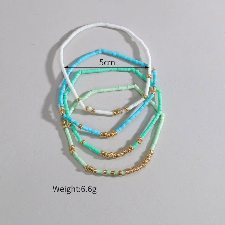 A set of four beaded headbands in white, light blue, mint green, and pastel green, arranged on a neutral gray background. A black line with &