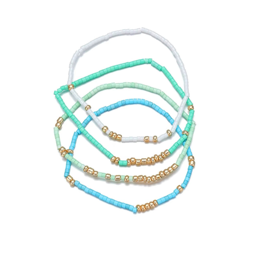 Five beaded stretch bracelets in pastel shades of white, mint green, light blue, and turquoise, accented with small gold spacer beads, arranged on a plain white background.