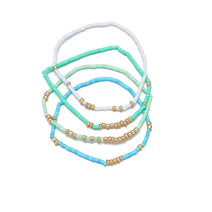 Five beaded stretch bracelets in pastel shades of white, mint green, light blue, and turquoise, accented with small gold spacer beads, arranged on a plain white background.