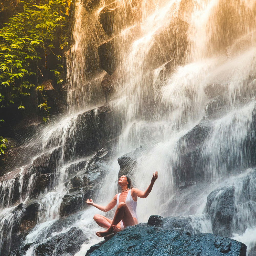 Woman meditating under waterfall, embracing spiritual healing and ascension energy in nature